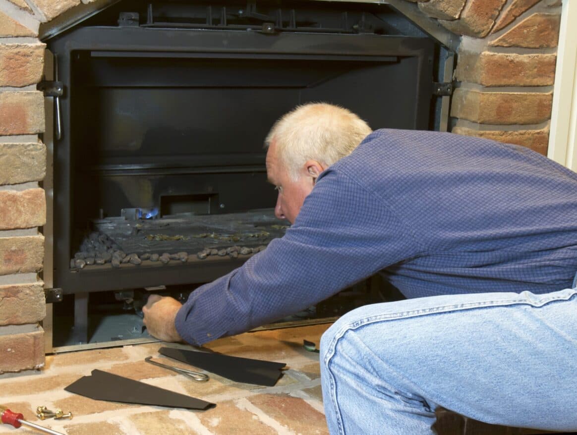 Technician reaching into an open gas firebox, tools on the hearth