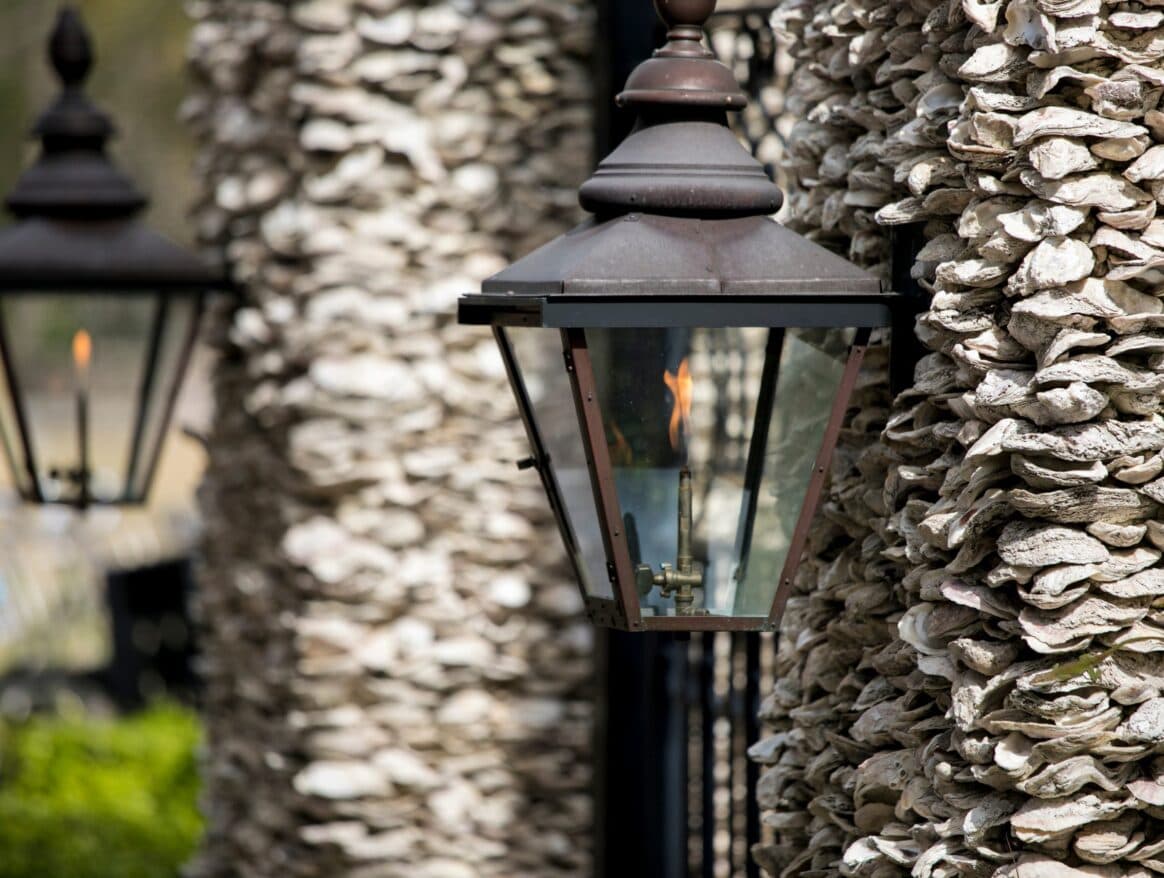 Copper gas lantern alight, mounted beside a shell-clad wall