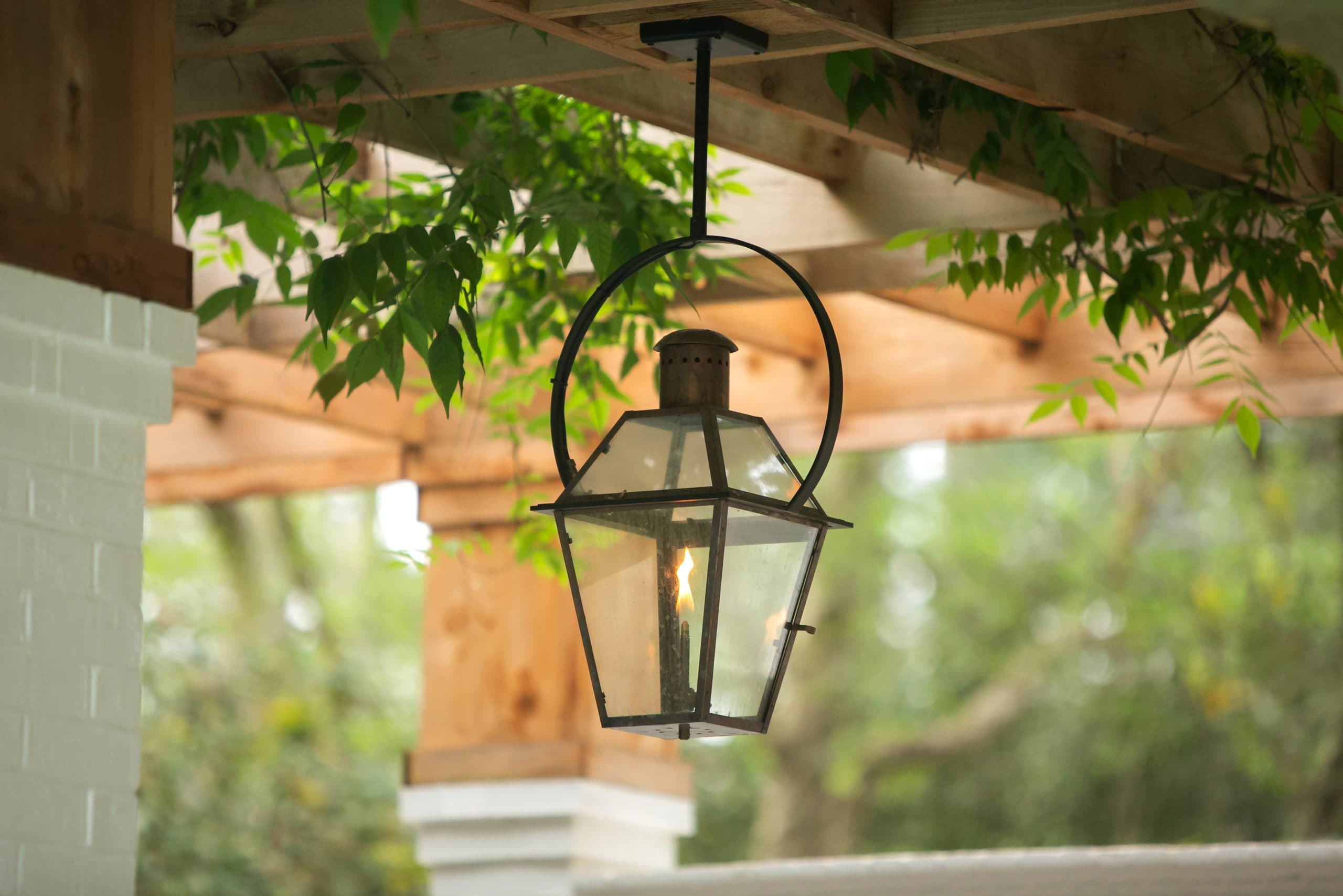 Gas lantern hanging from a timber pergola, flame alight