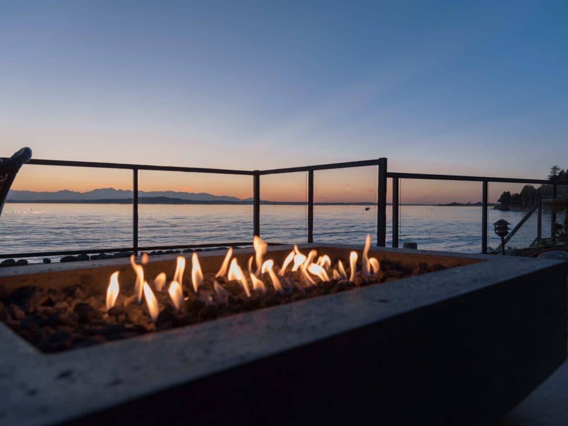 Concrete gas firepit alight on a deck overlooking the water