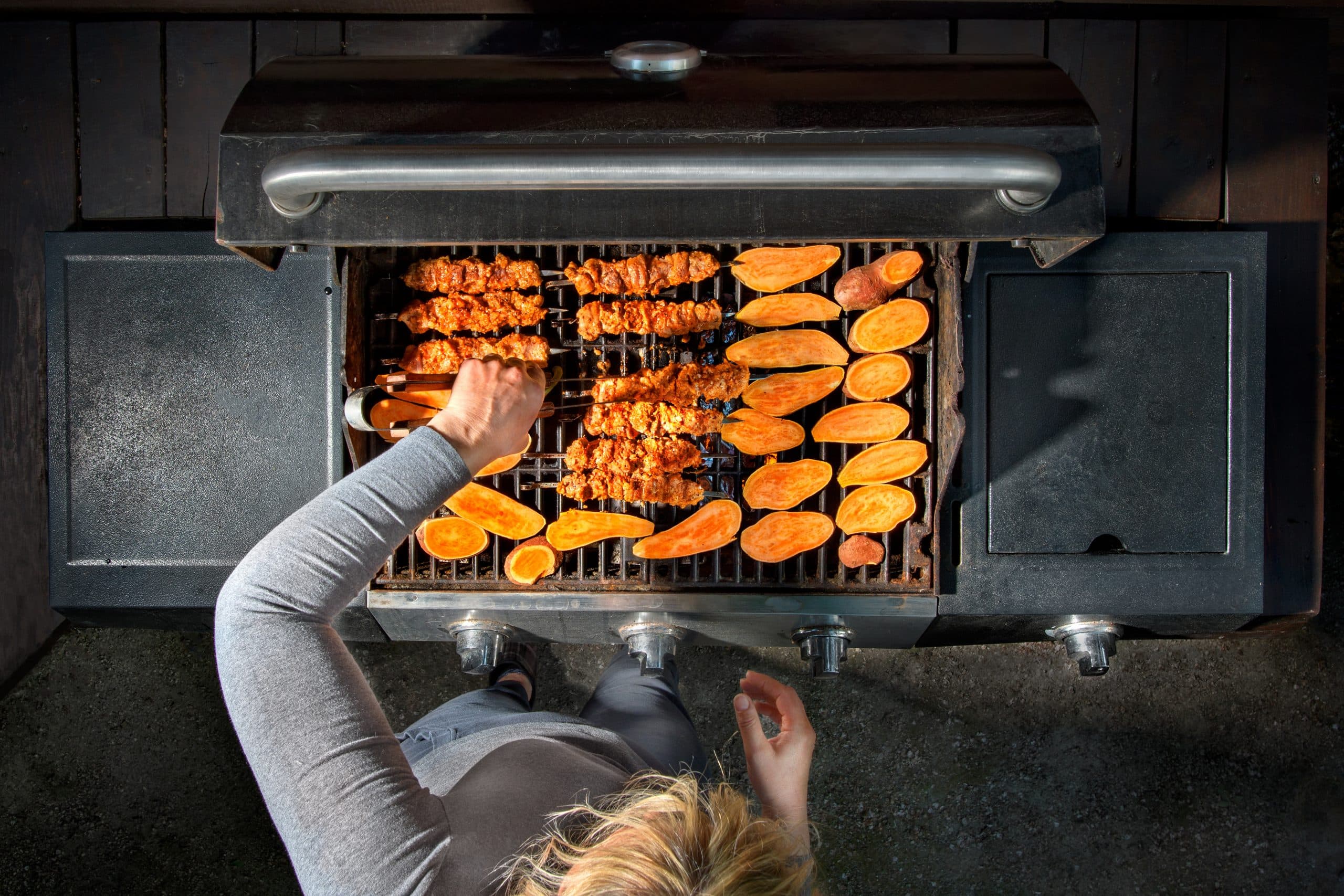 Skewers and sweet potato cooking on a gas grill, seen from above